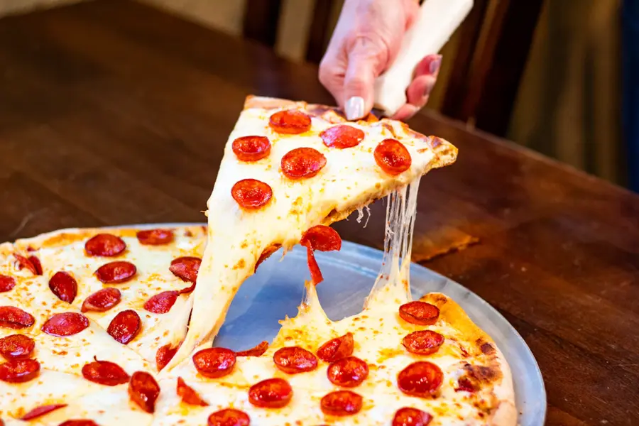 Fatia de pizza pepperoni New York style com queijo derretido, servida ao corte